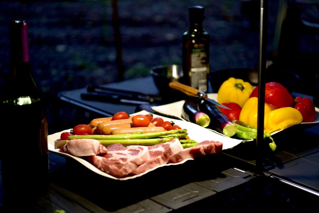 夜のキャンプテーブルに並べられた肉や野菜などの豪華なキャンプ料理の食材