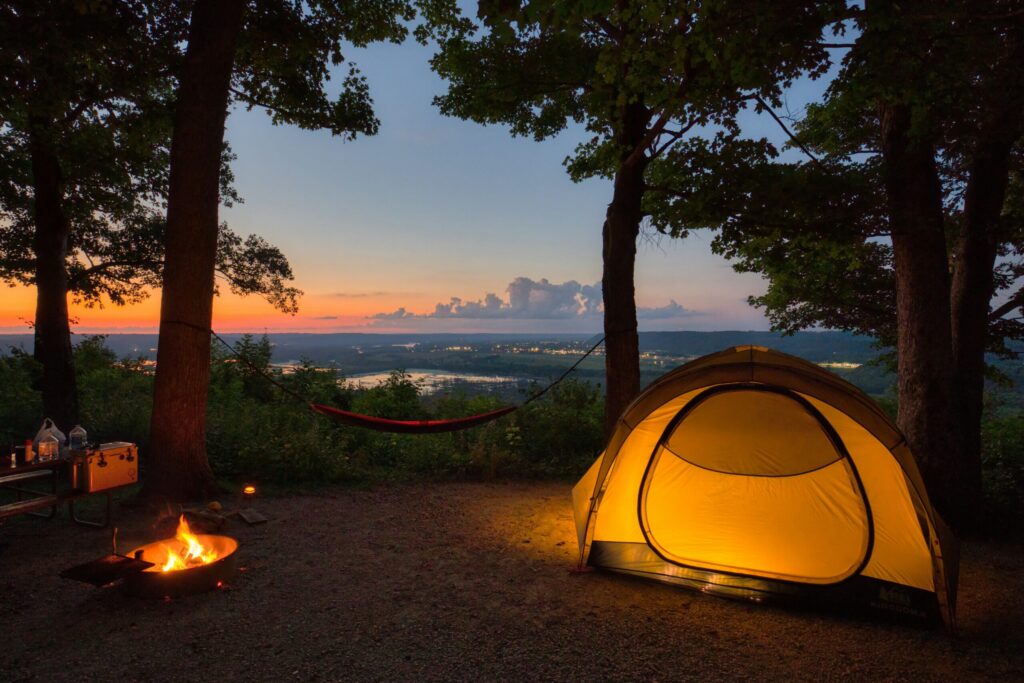 夕暮れの森でライトが灯るテントと焚き火、ハンモックがあるソロキャンプの風景