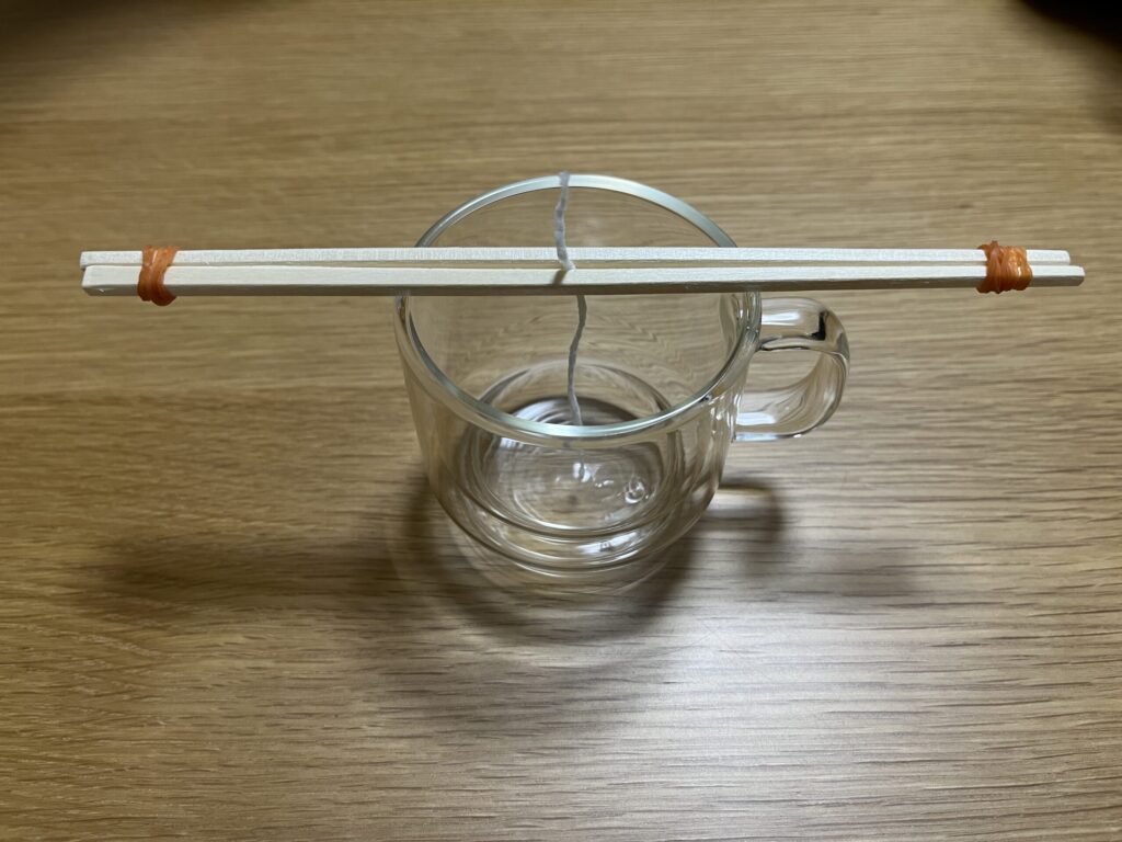 ガラス容器にキャンドル芯を固定し、割り箸で位置を調整している様子。