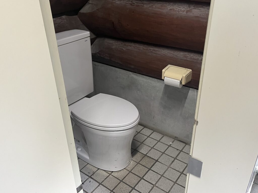 高間木キャンプ場のログハウス風トイレ内部。洋式便器が設置された清潔な個室。