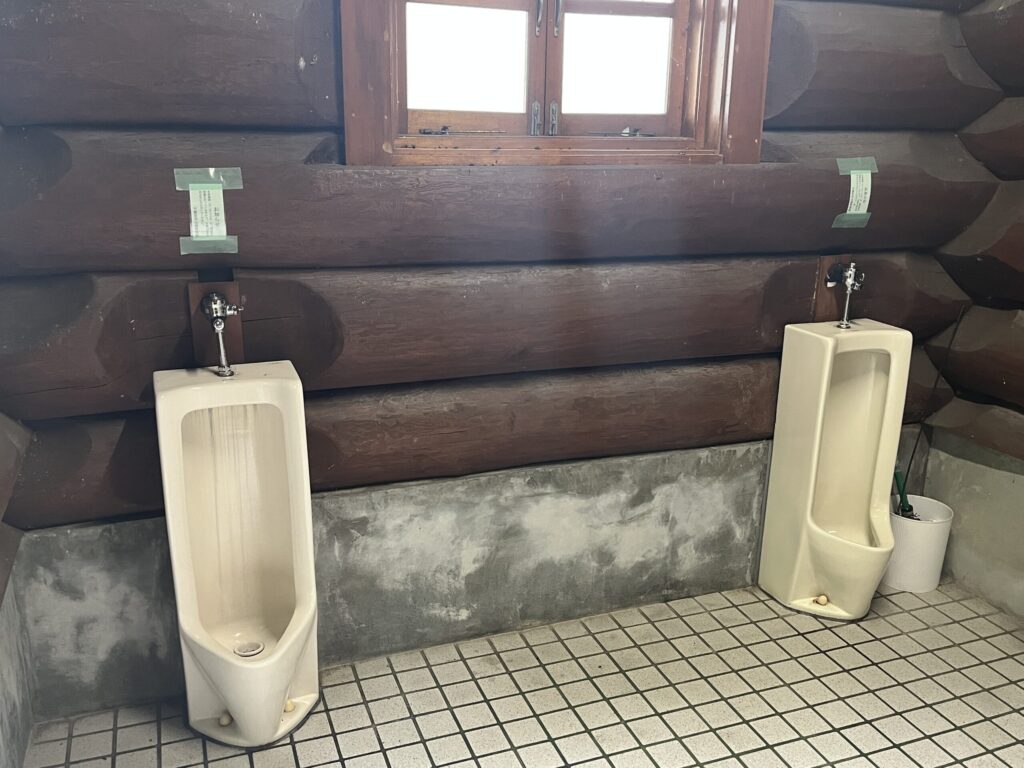 高間木キャンプ場のログハウス風トイレ内部。小便器が設置された男性用トイレ。