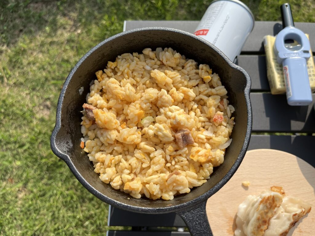 スキレットで作ったチャーハンをソロキャンプで楽しむ様子。青空の下で餃子と一緒に味わうキャンプ飯。