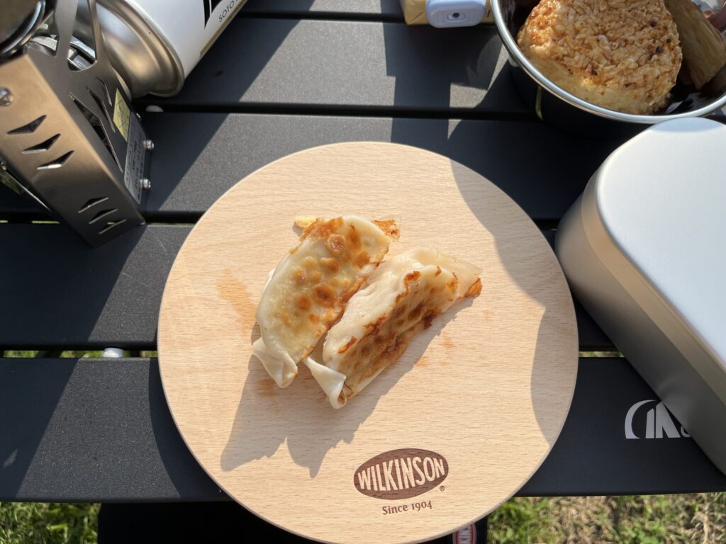 ソロキャンプで焼いた焼き餃子を木製プレートに盛り付けた写真。手軽に楽しめるキャンプ飯。